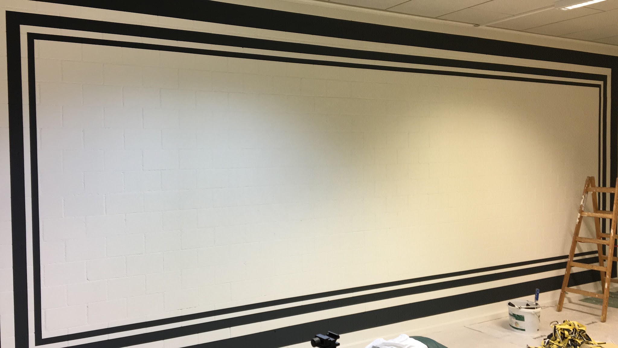 Weisse Wand mit dunkler Bordüre und Malerleiter